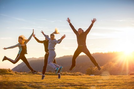 Group of friends running happily together in the grass and jumping